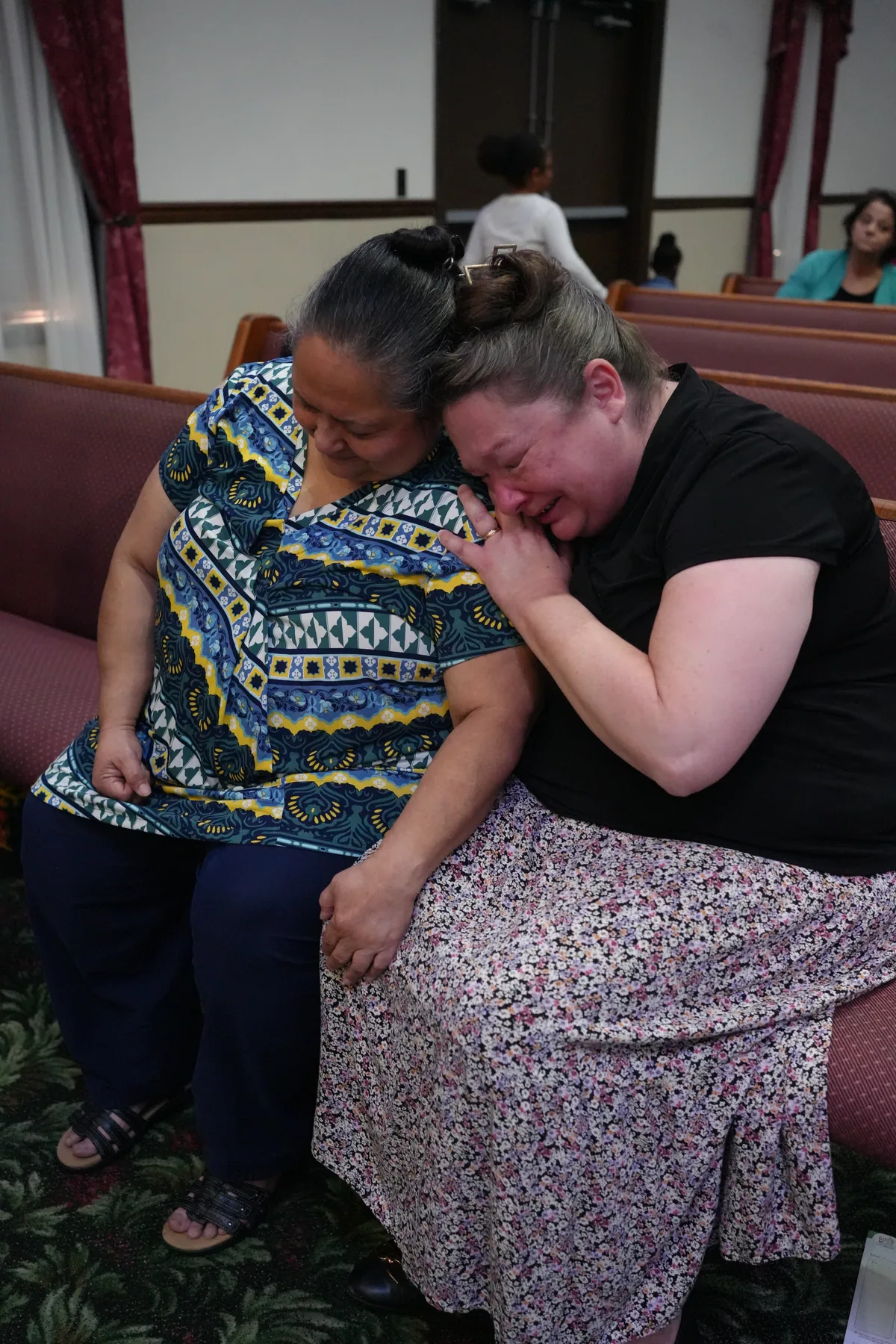 Two women sitting together in a pew, one holding the other