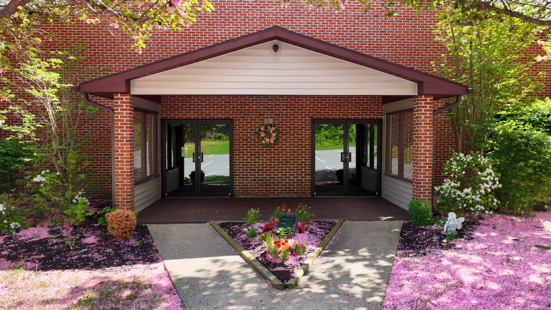 The brick entrance of Bethel Christian Center: a gabled porch, glass doors, a wreath, and two flowering trees