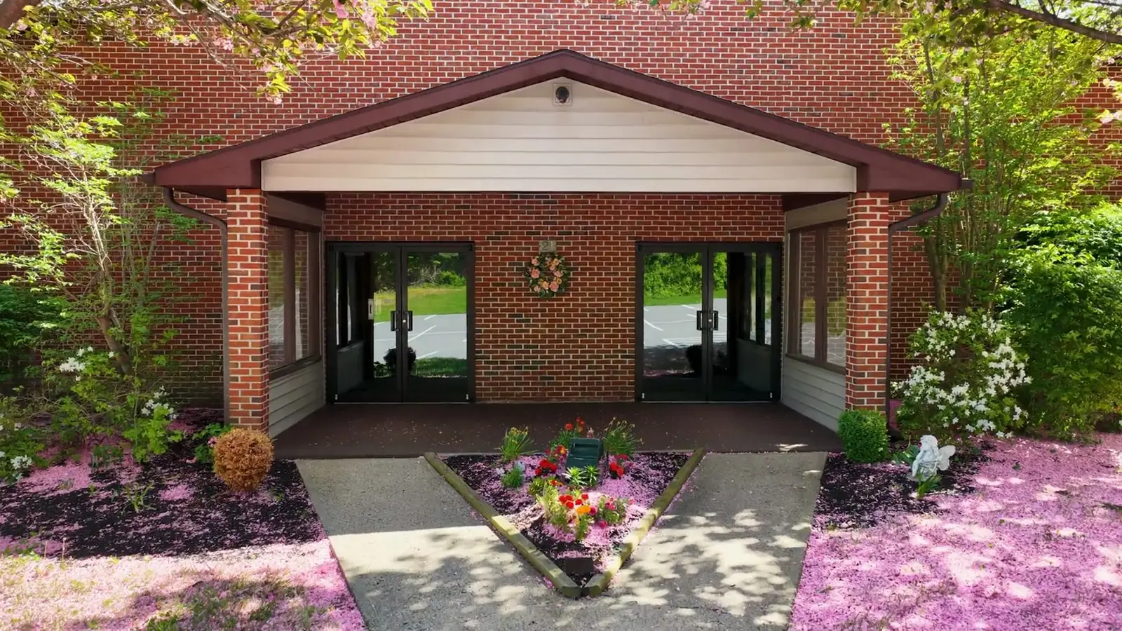 The brick entrance of Bethel Christian Center, its doors under a gable, between two flowering trees